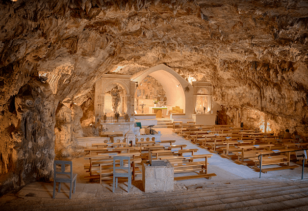 Church interior built inside a natural cave with wooden pews and illuminated altar