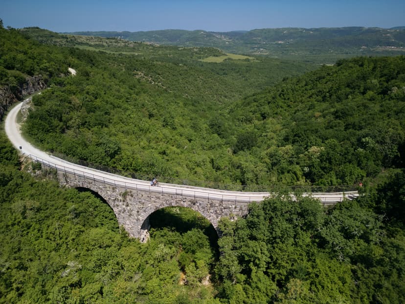 Cyclist riding on the Parenzana trail viaduct over lush green valley landscape.