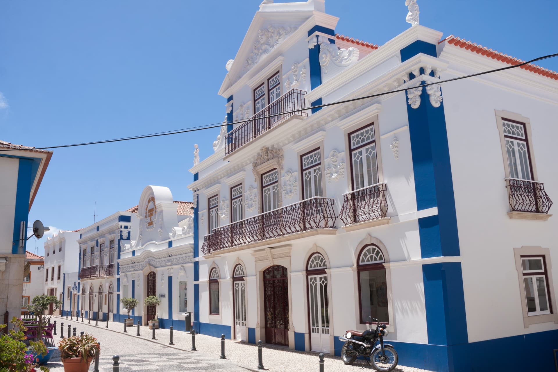 White and blue ornate building facade on a sunny cobblestone street in Ericeira.