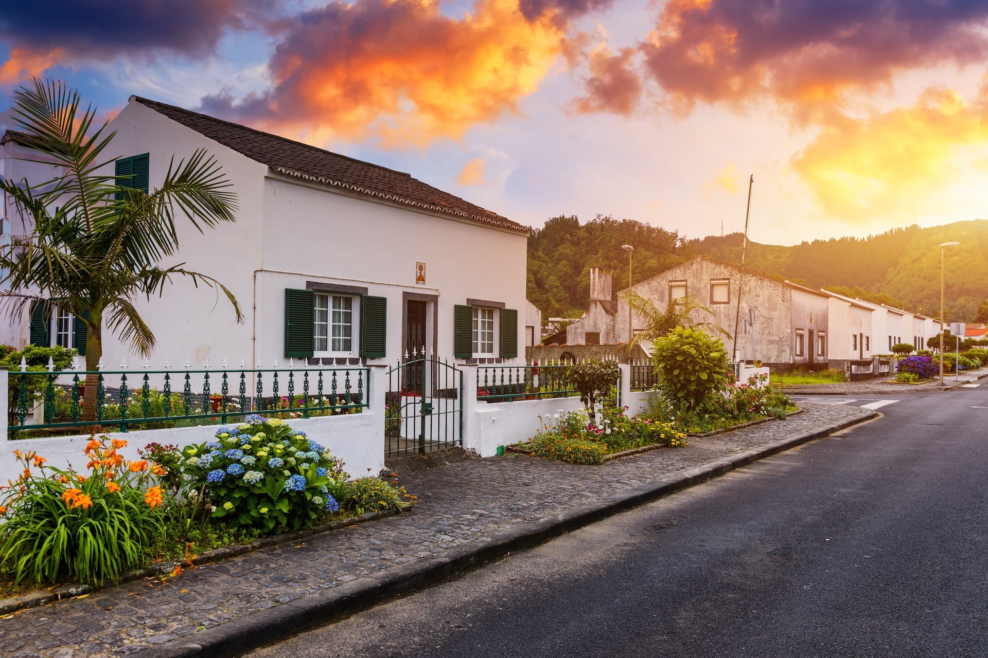 White houses with green shutters along a street in Sete Cidades village under a dramatic sunset.