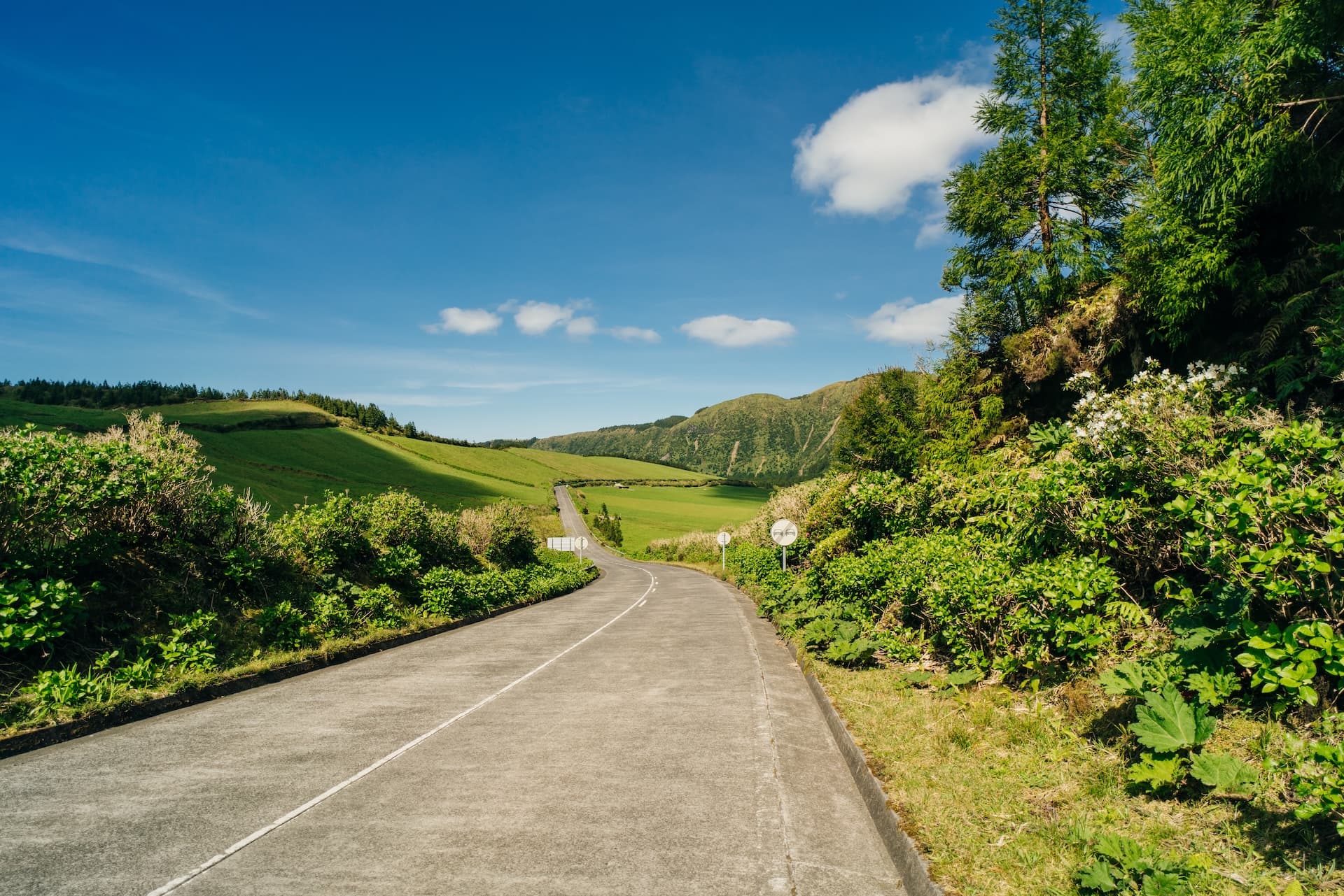 Winding road through lush green hills under a bright blue sky, Road to Sete Cidades