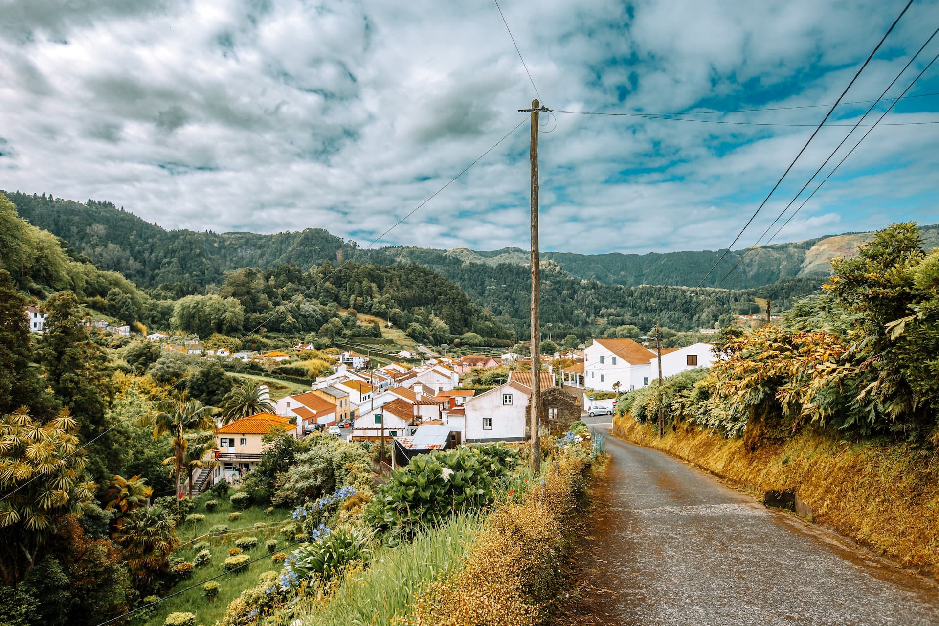 Winding road leading into Furnas village nestled among lush green mountains under a cloudy sky.