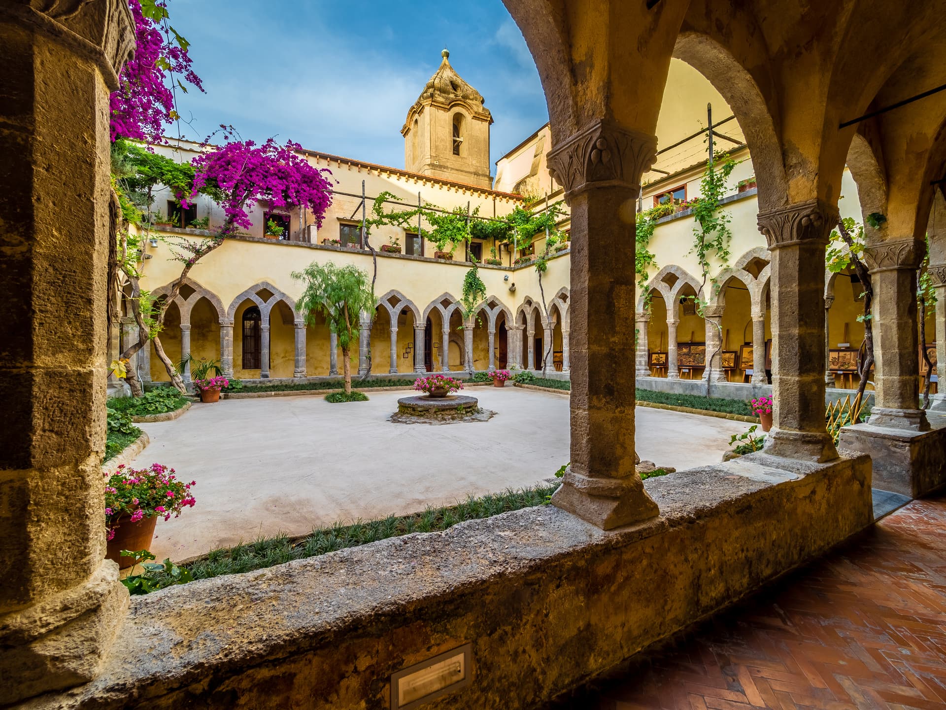 Cloister courtyard of Sorrento monastery with arcades, bell tower, and purple bougainvillea.