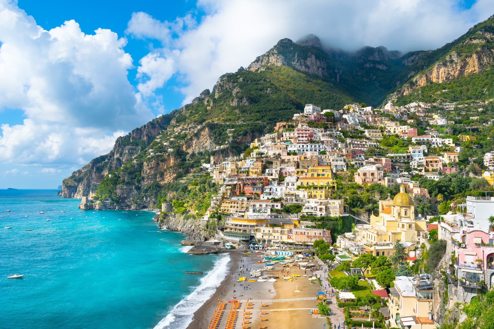 Colorful houses cascade down cliffs above a beach with orange loungers and turquoise sea in Positano.