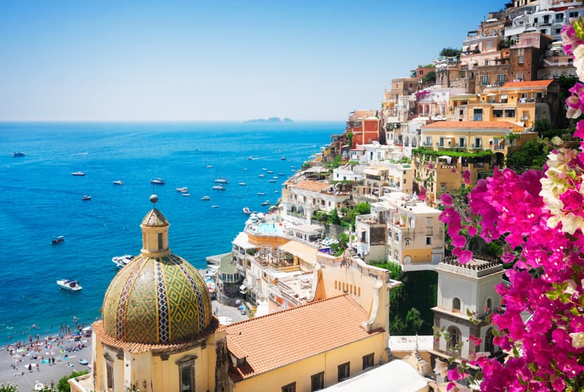 Colorful tiled dome church overlooking Positano beach, Amalfi Coast, with boats on blue sea.