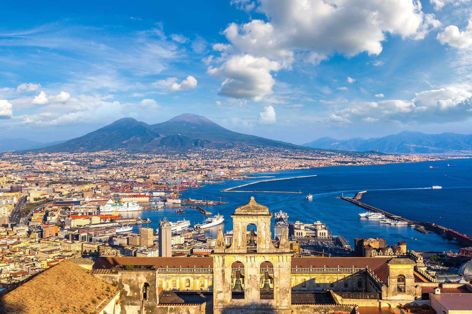 Naples cityscape with historic church foreground and Mount Vesuvius overlooking the bay.