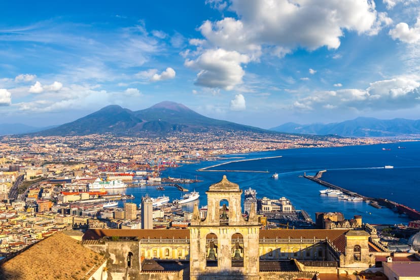 Naples cityscape with historic church foreground and Mount Vesuvius overlooking the bay.