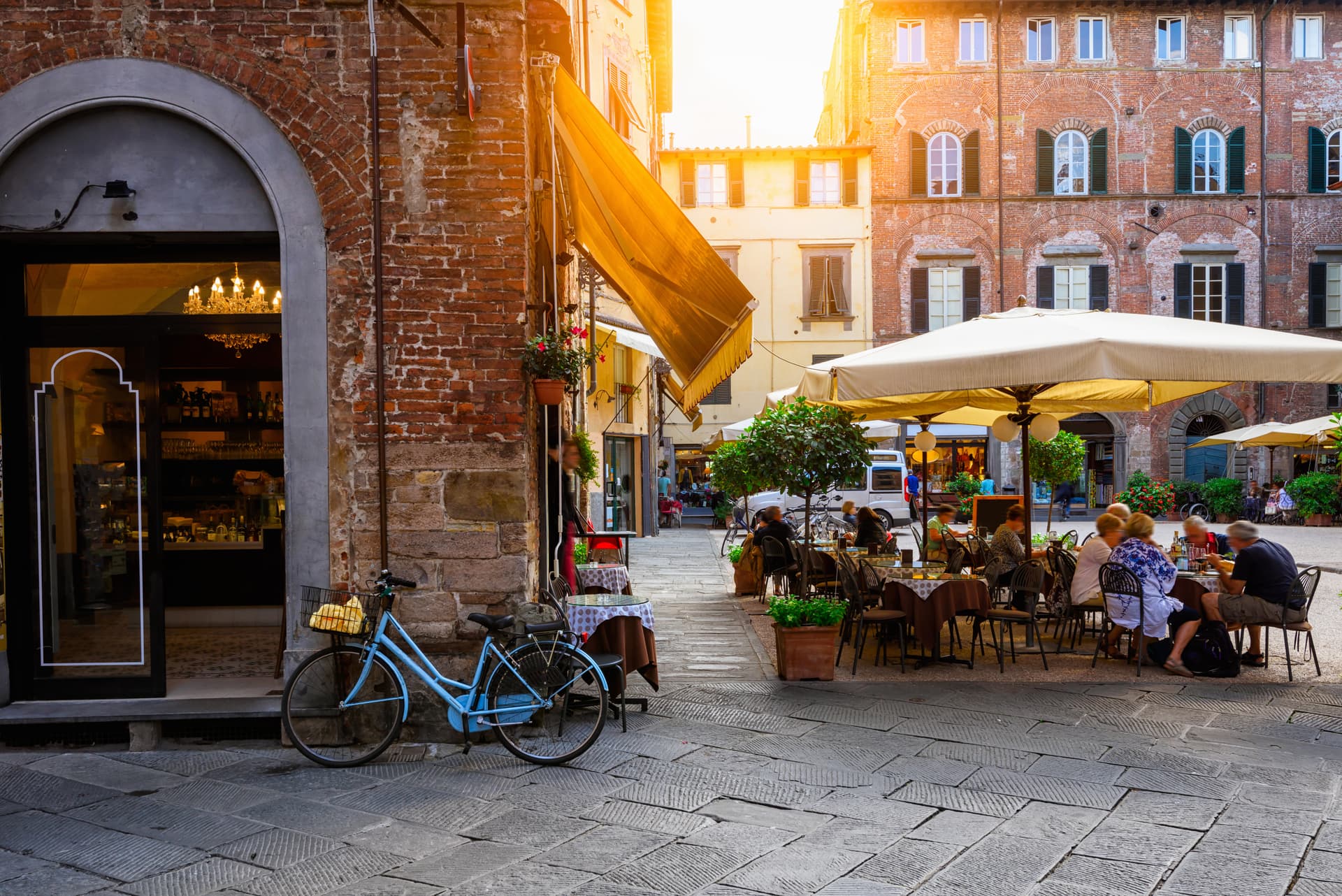 Blue bicycle parked near outdoor cafe seating in Italian city square with brick buildings.