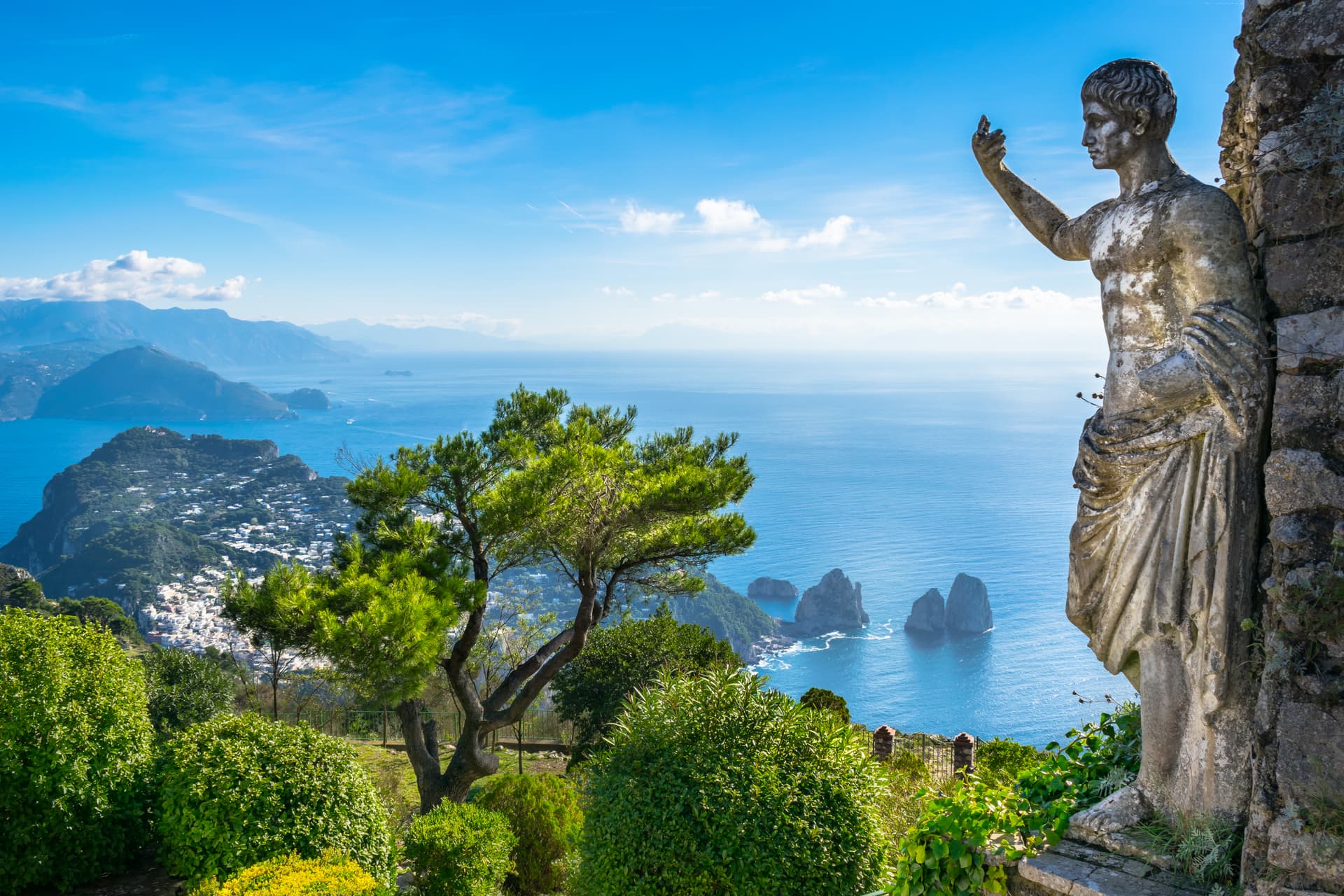 Stone statue overlooking the sea, town, and Faraglioni rocks on Capri.