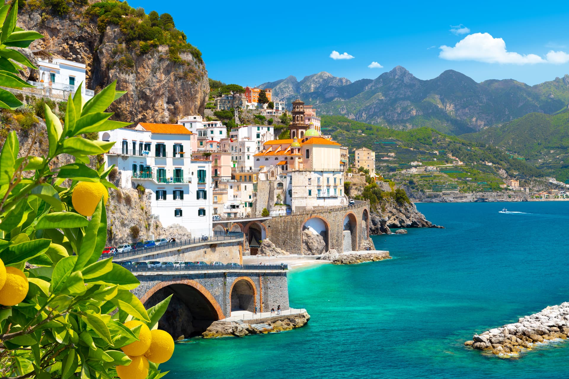 Lemon branch frames colorful buildings on cliffside above turquoise sea in Atrani, Amalfi Coast.