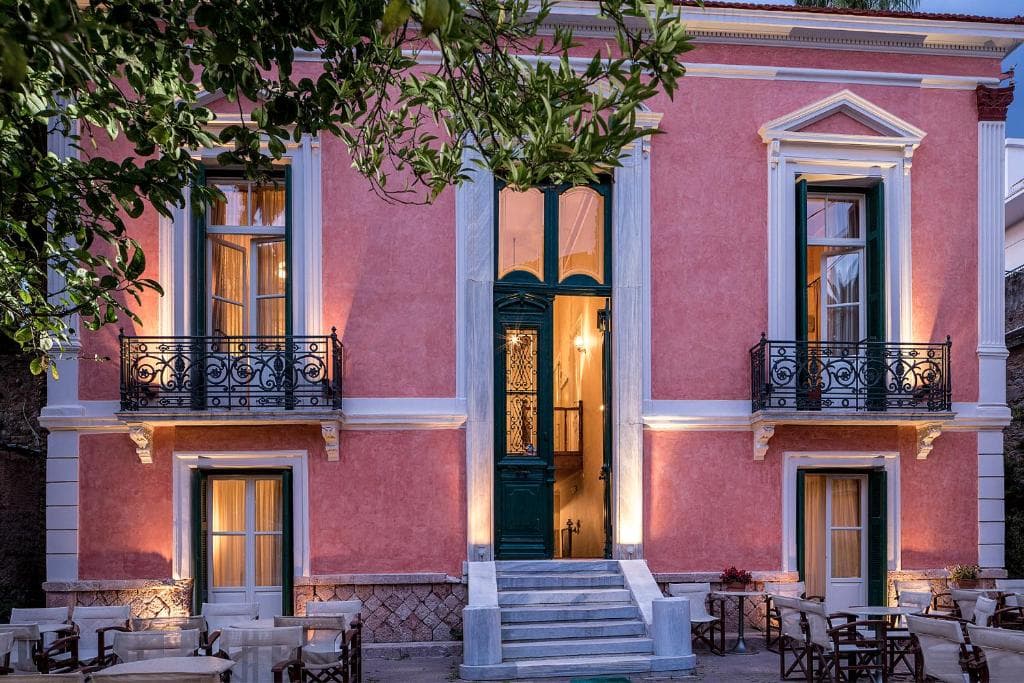 Pink neoclassical building with white marble trim and outdoor cafe seating at dusk.