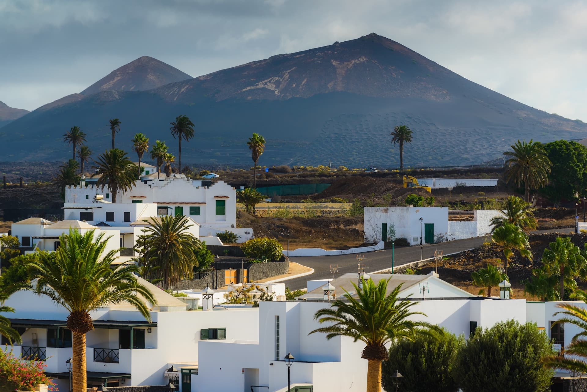 White buildings and palm trees in Lanzarote, Canary Islands, with volcanic mountains in the background.