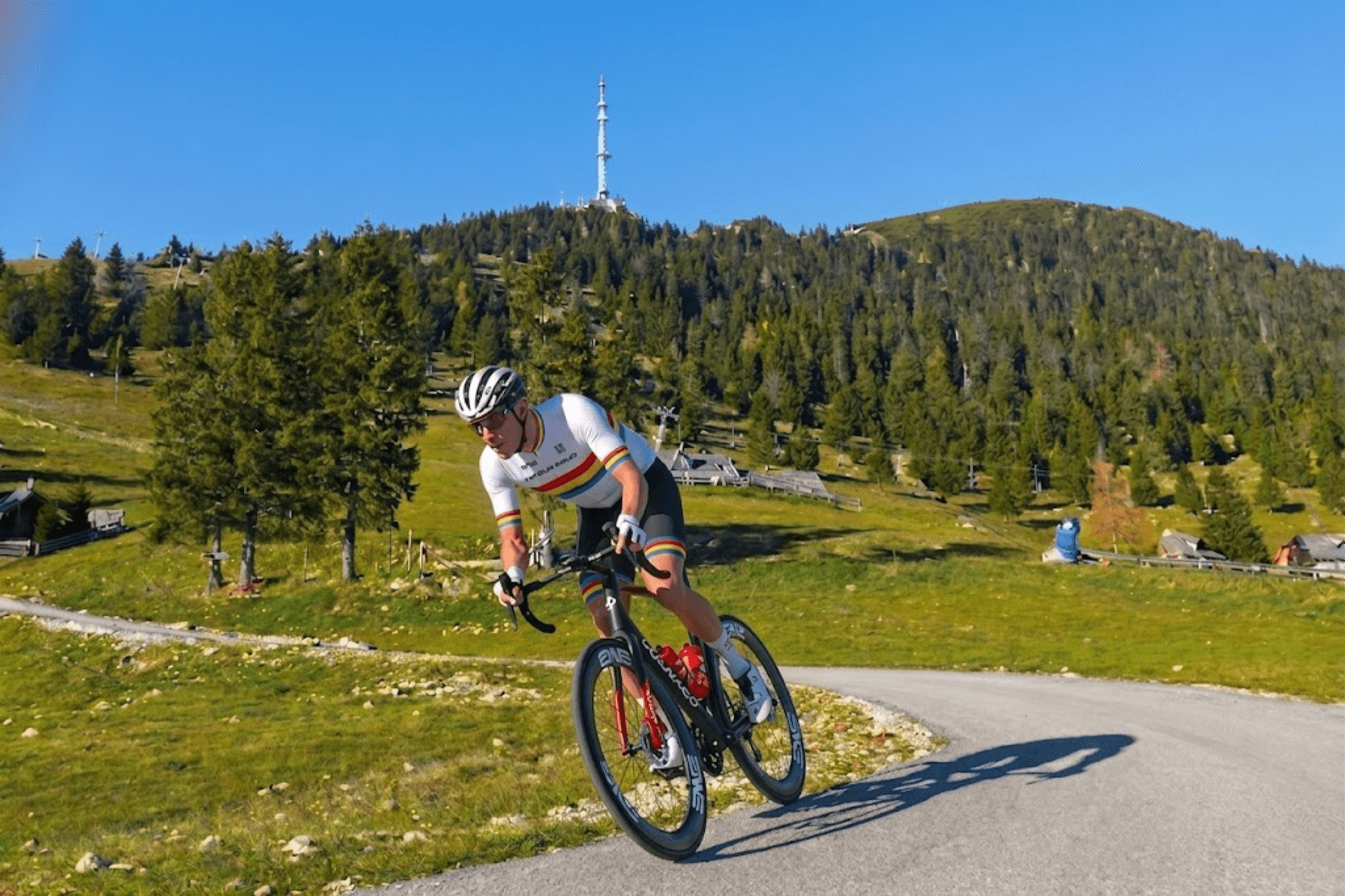 Cyclist riding on a mountain road with a communications tower on the peak in the background.