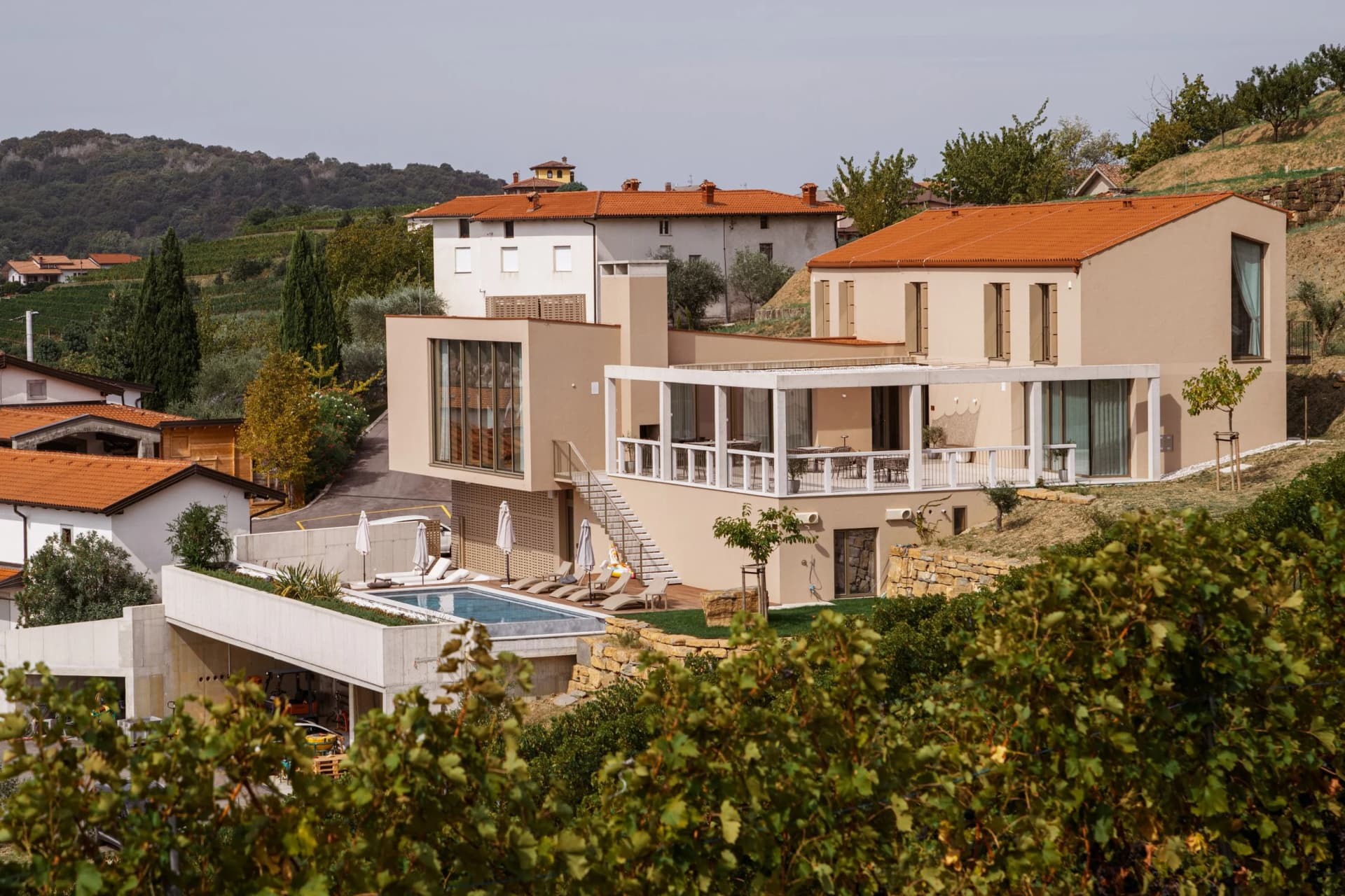 Modern villa with swimming pool and terrace overlooking a vineyard in a hilly landscape.