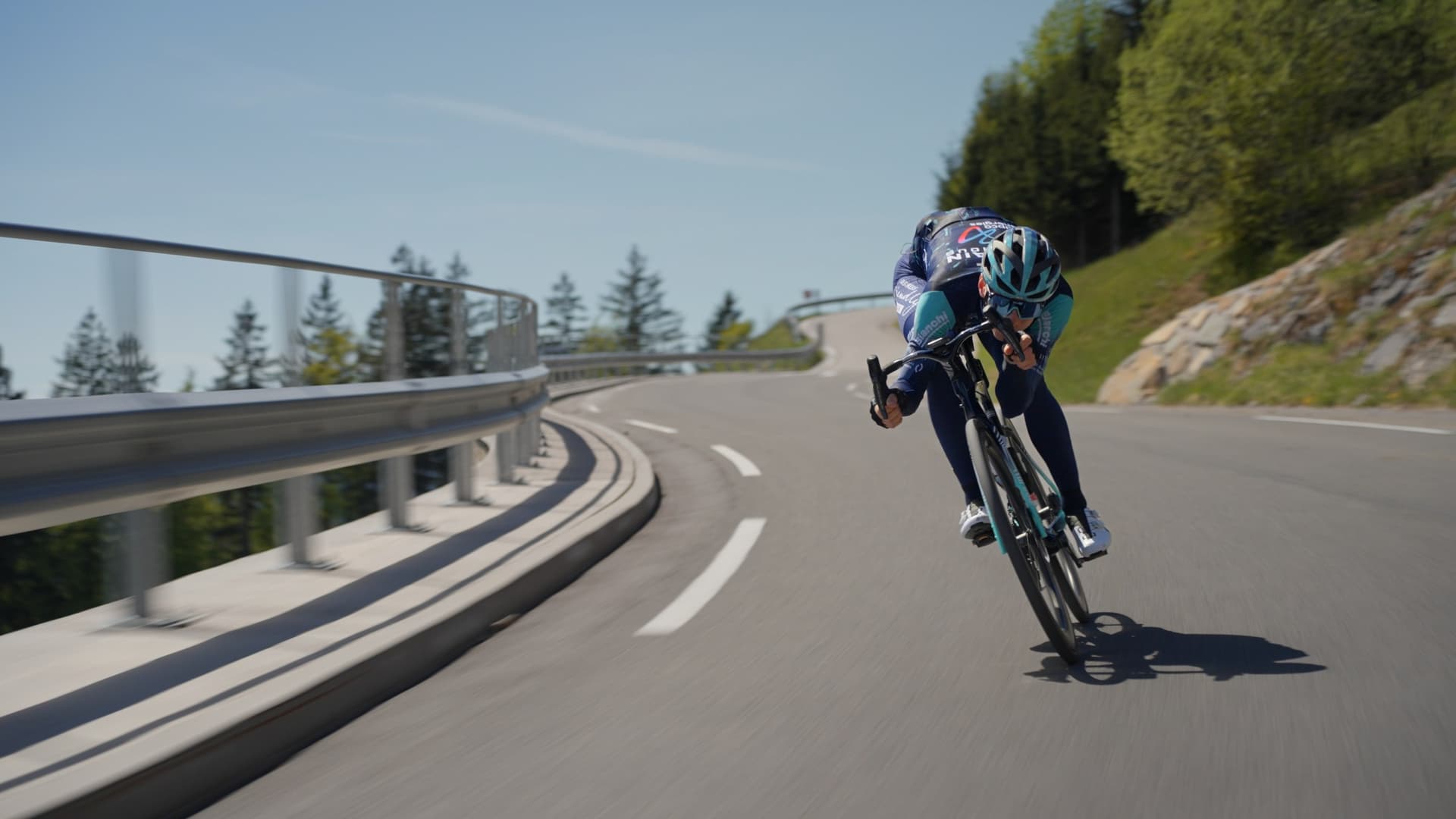 Cyclist descending a mountain hairpin turn on a paved road.