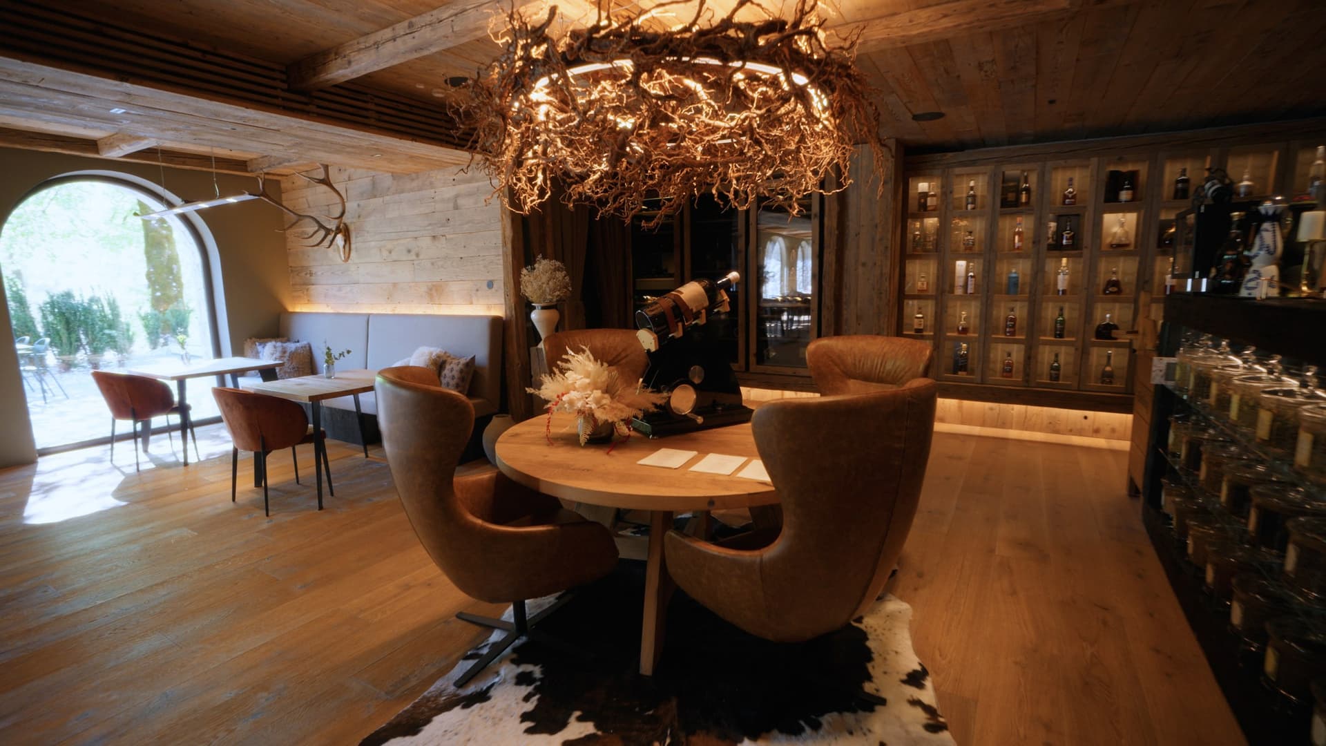 Chalet dining room with antler chandelier, leather armchairs, and wooden interior.