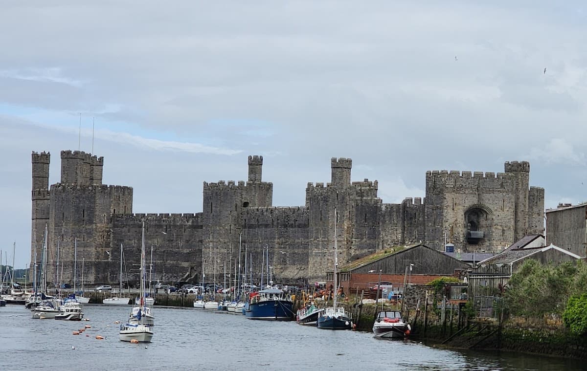 Caernarfon Castle with stone walls and towers overlooking a harbor full of moored sailboats and boats on the water