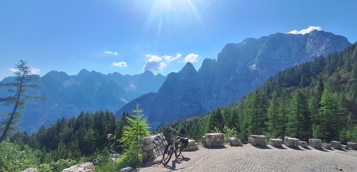 Bicycle parked on cobblestone mountain road with pine forest and alpine peaks under bright sun