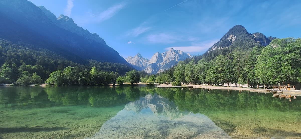 Alpine lake with crystal-clear water reflecting surrounding mountains and green forests under a blue sky
