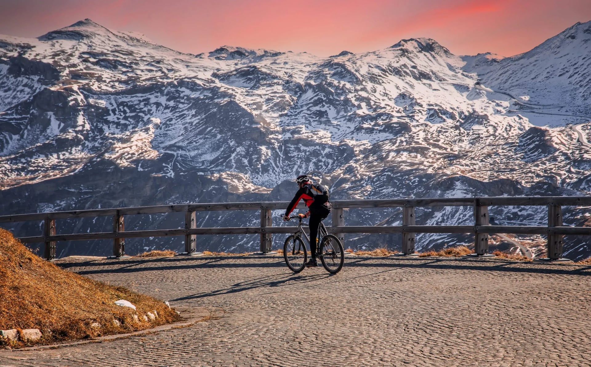 Cyclist on cobblestone road overlooking snow-capped mountains at sunset
