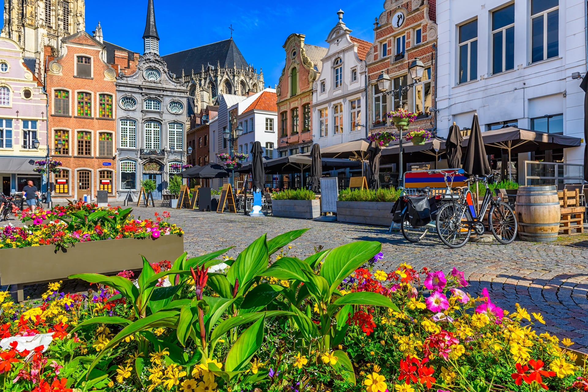 Cobblestone square with colorful flowers, historic buildings, and outdoor cafe seating in Brussels or Bruges.