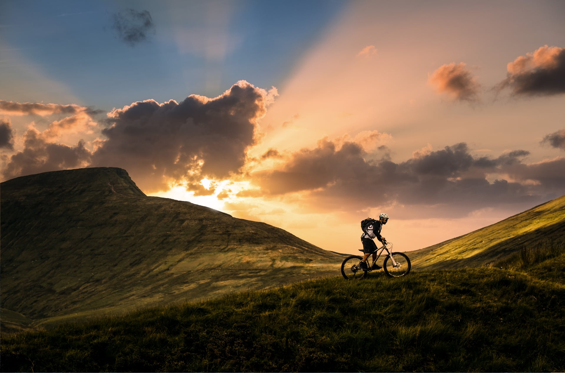Mountain biking on grassy hills at sunset in Wales with dramatic clouds.
