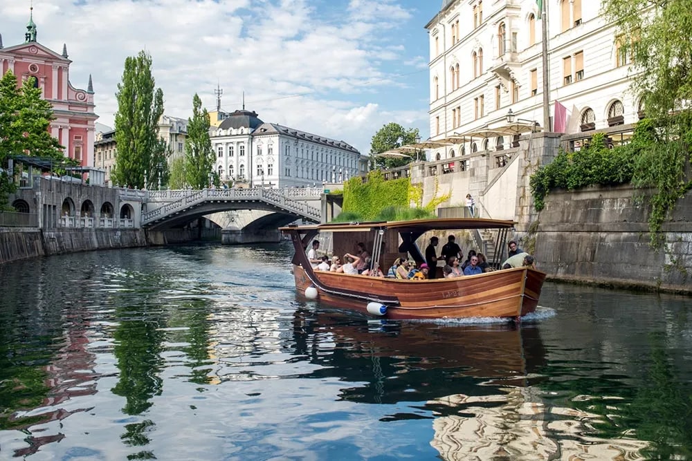 Wooden tourist boat with passengers cruising the Ljubljanica River in Ljubljana.