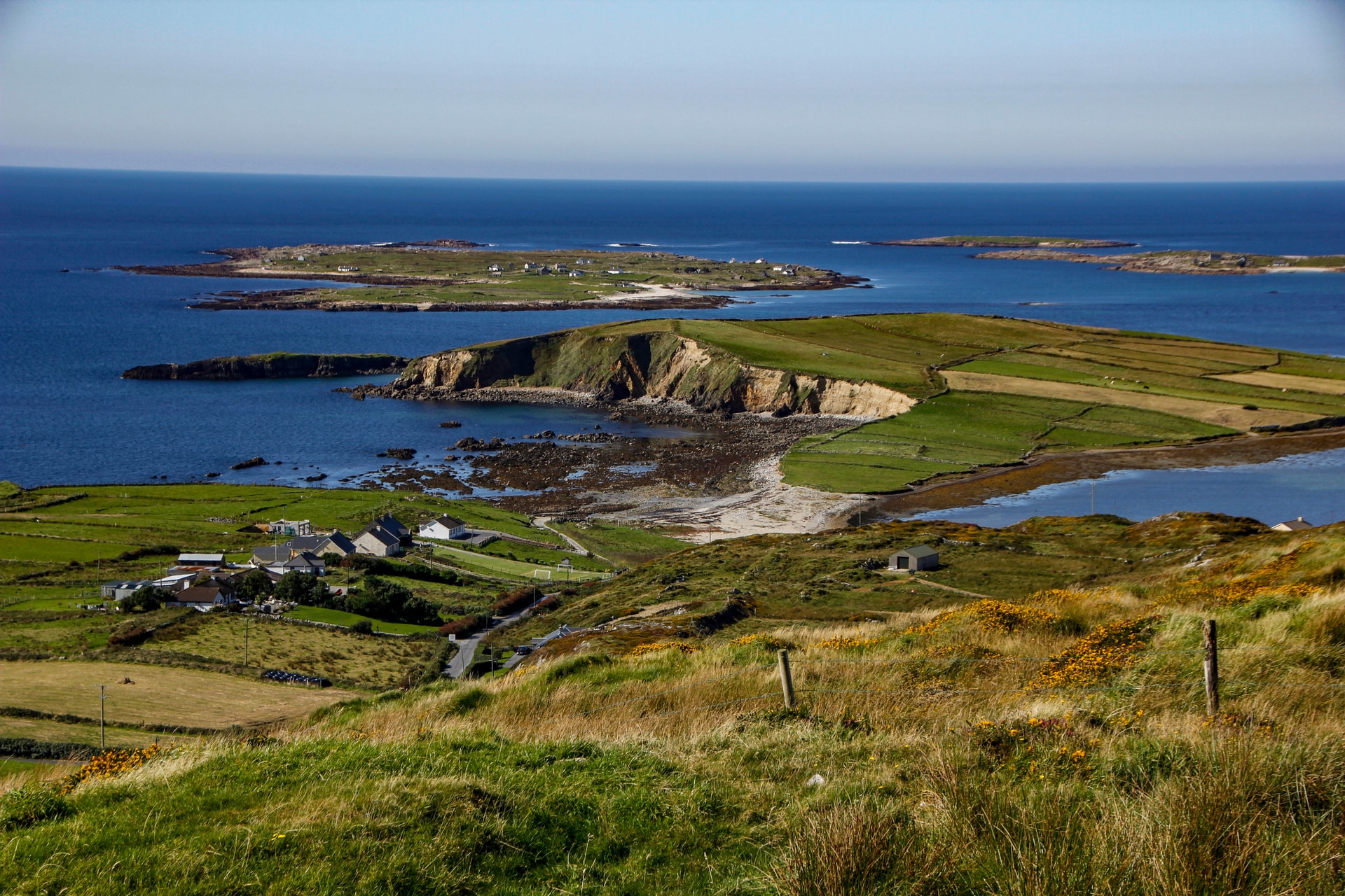 Scenic drive near Clifden showing green fields, coastal cliffs, and islands in the blue Atlantic Ocean.