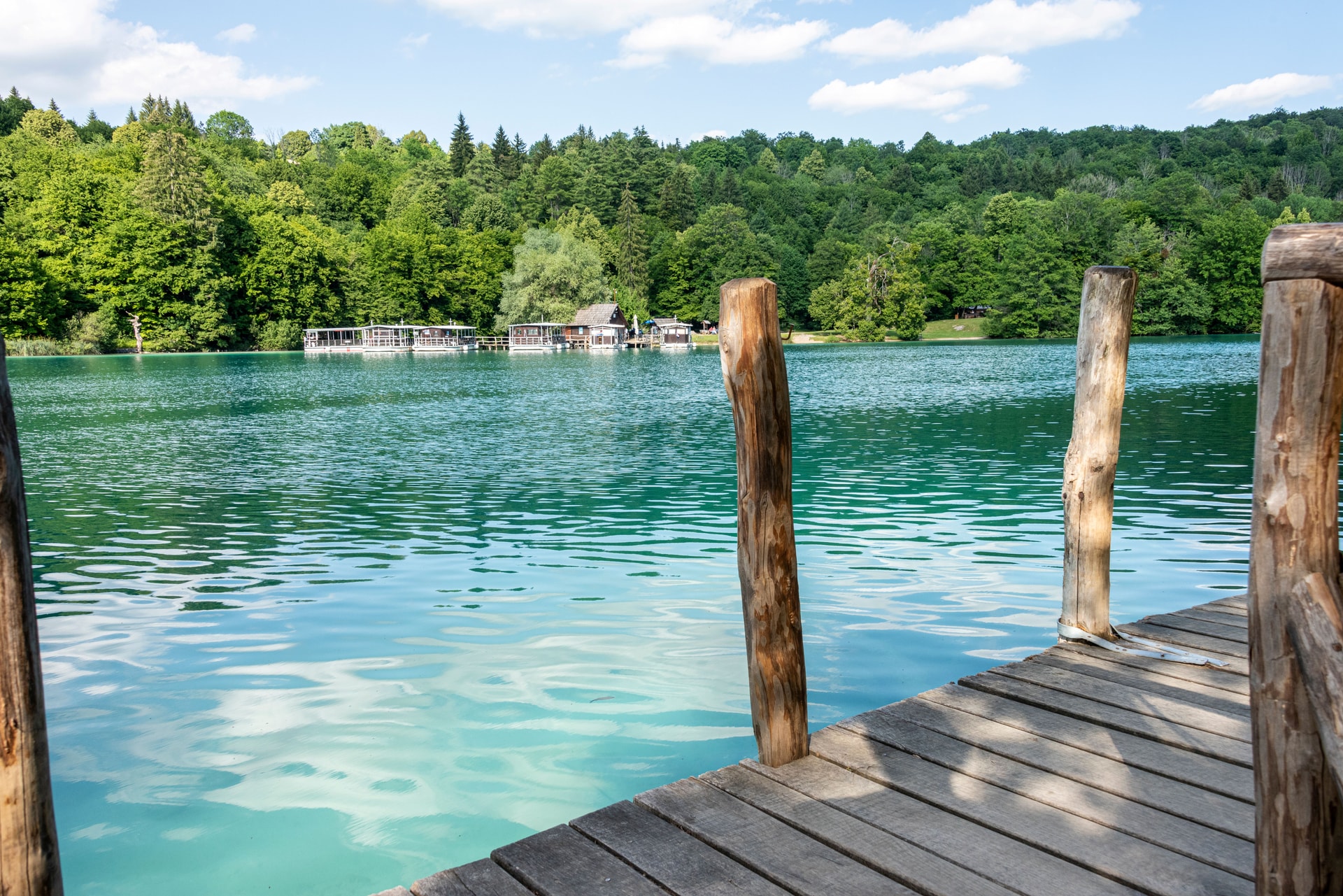 Wooden pier on turquoise lake with floating cabins and dense green forest.