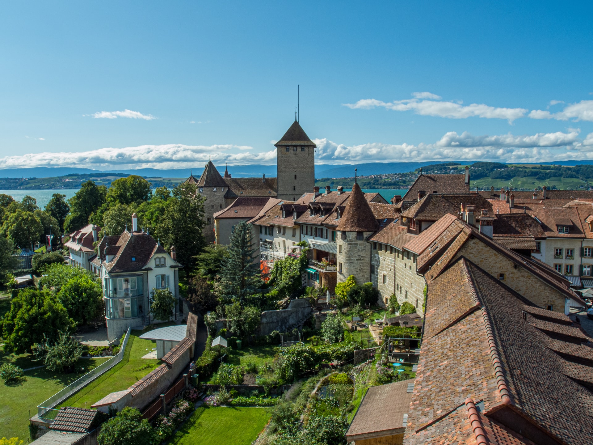 View of Murten castle tower and historic town roofs overlooking a lake and distant hills.