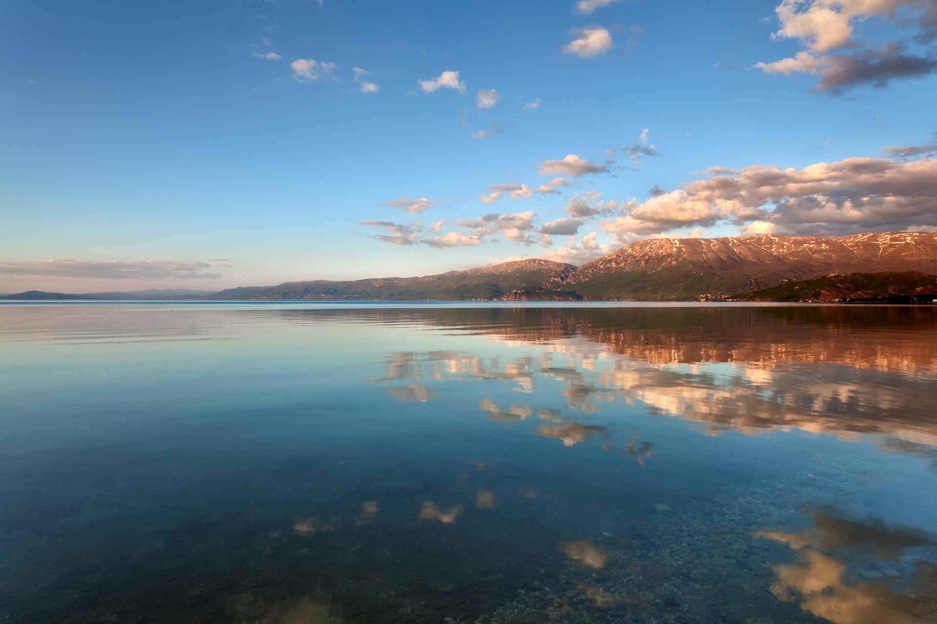 Calm Lake Ohrid, Albania, reflecting mountains and sunset clouds.