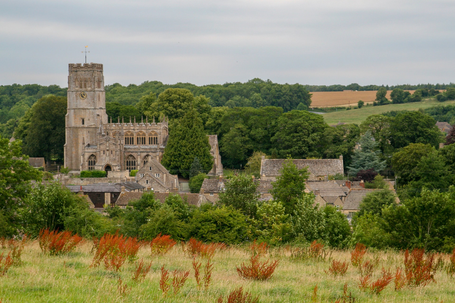 Stone church tower overlooking village houses surrounded by lush green trees in Northleach.