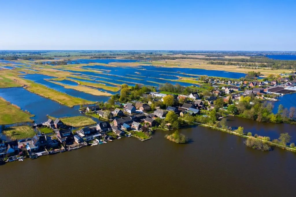 Aerial view of Nieuwkoop village surrounded by polders and dark water under a clear blue sky.