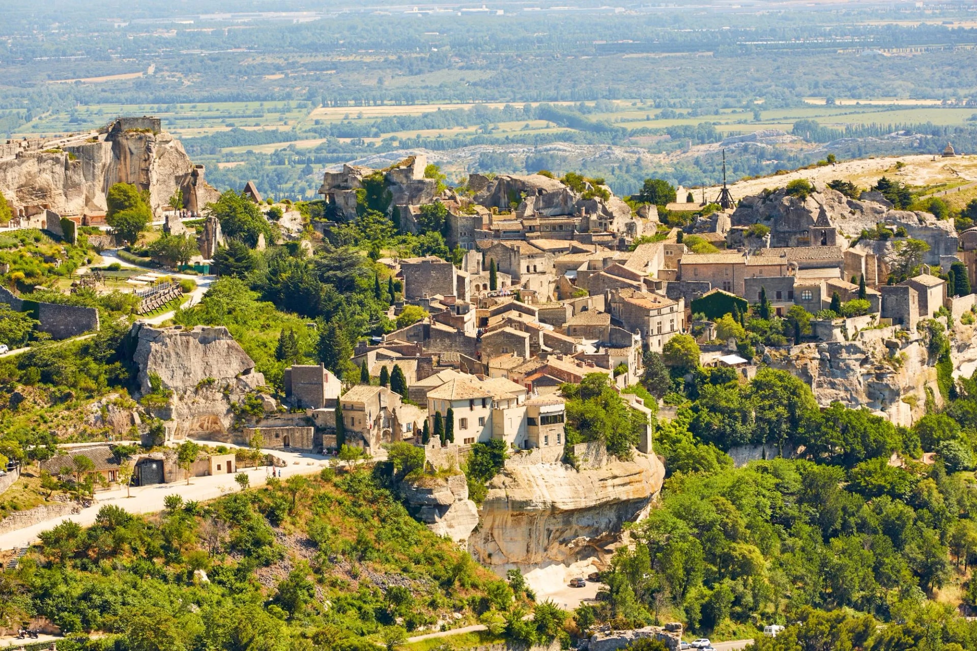 Historic village of Les Baux-de-Provence perched on rocky cliffs above green valley.