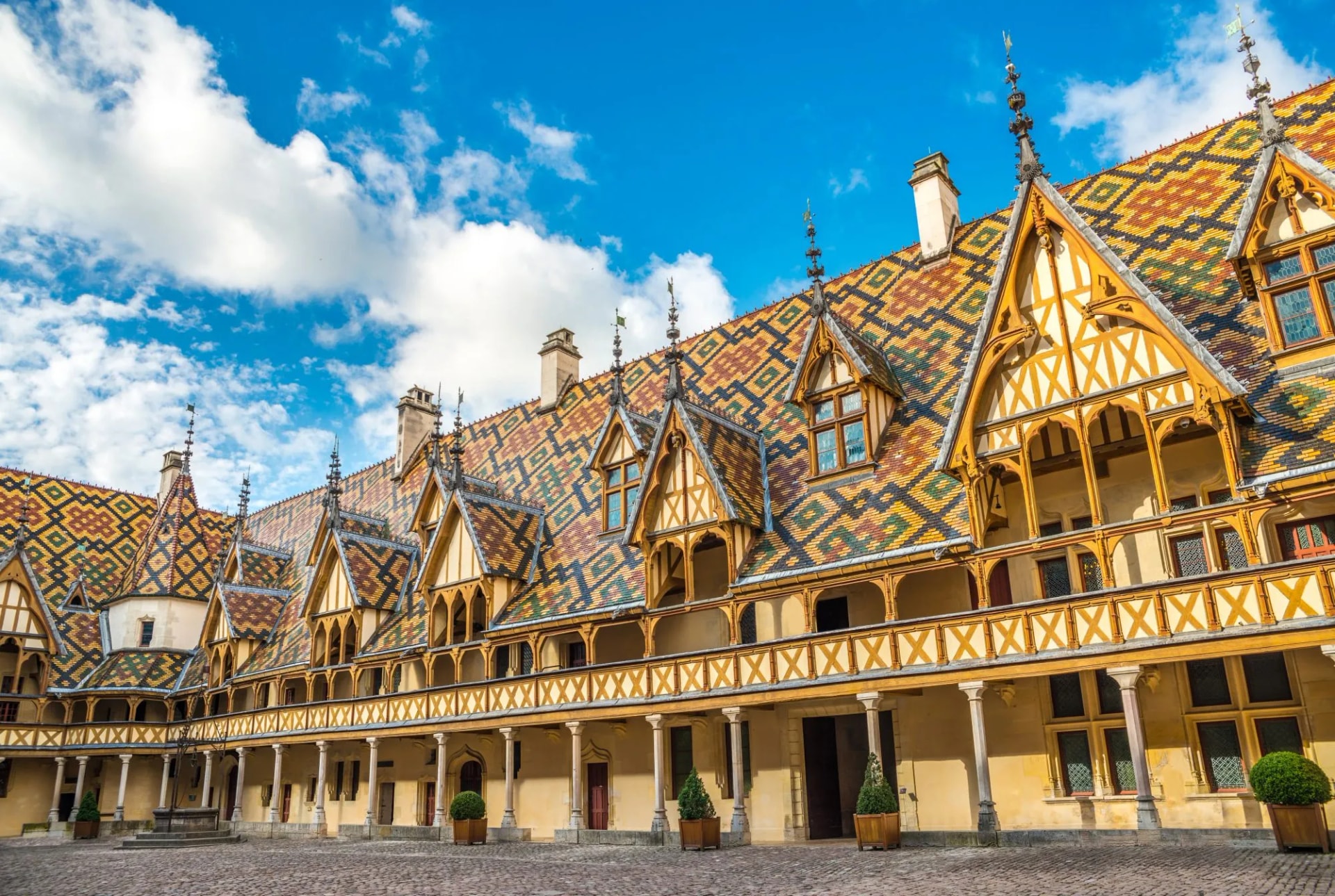 Hospices de Beaune courtyard with colorful tiled roof under a bright blue sky.