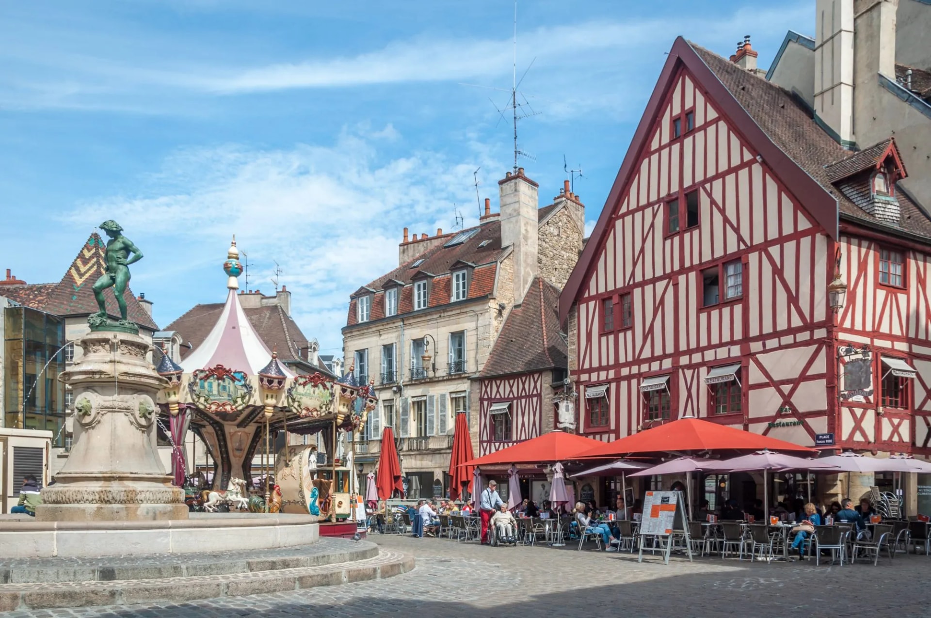 Fountain, carousel, and outdoor cafe seating near half-timbered building in Burgundy.