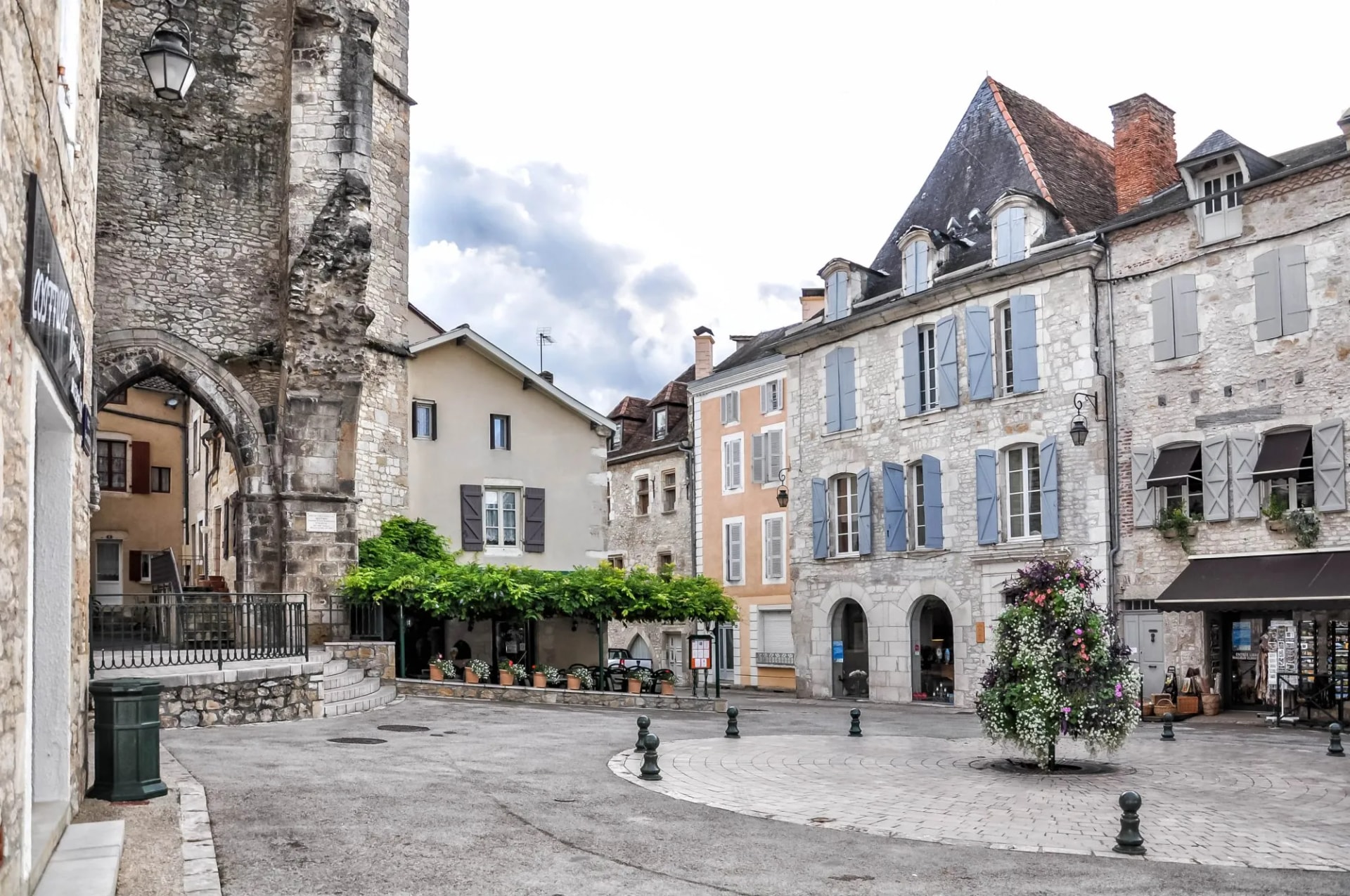 Stone archway and historic buildings around a paved square in Souillac town center.