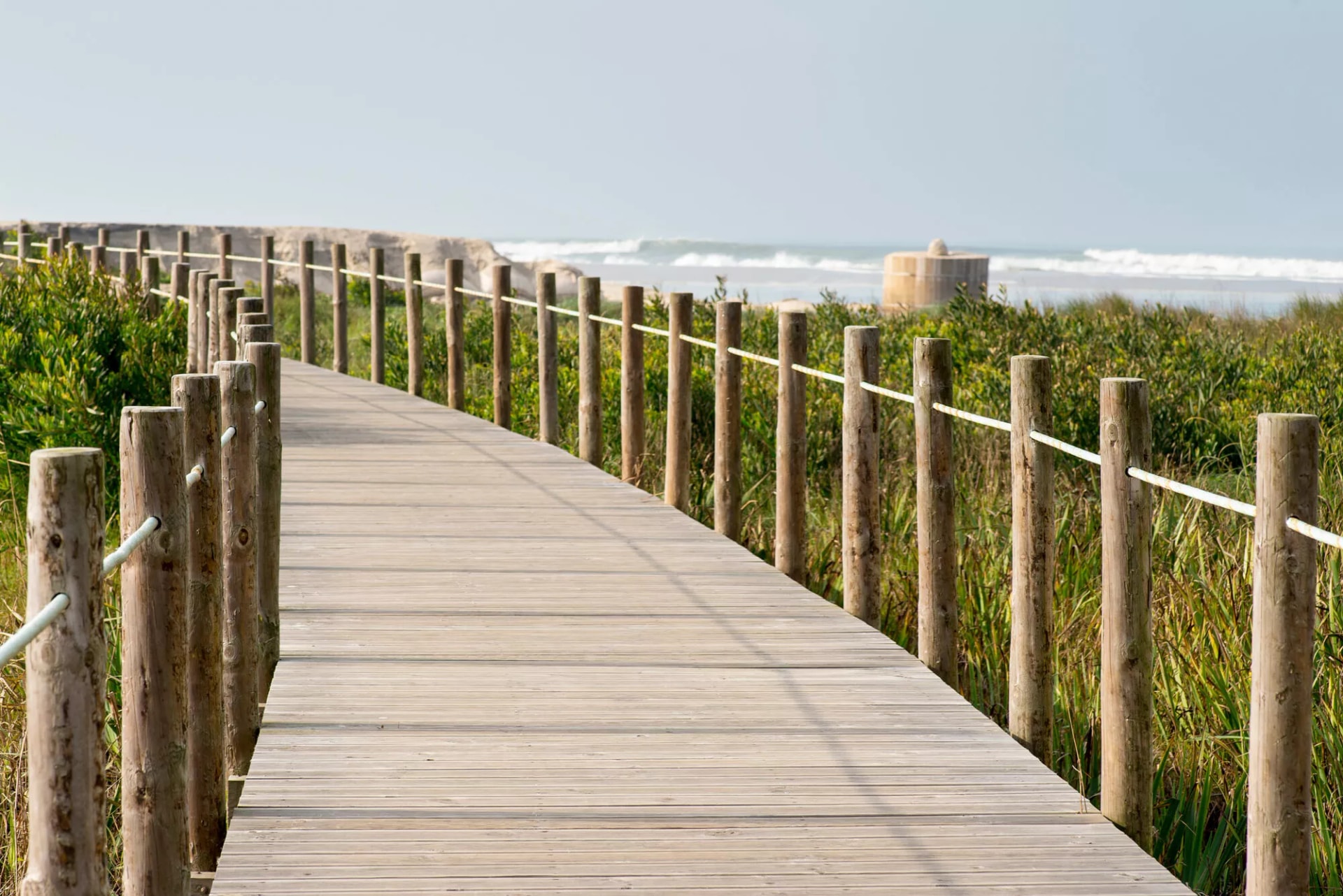 Wooden walkway curving through green coastal vegetation toward the ocean at Barrinha.