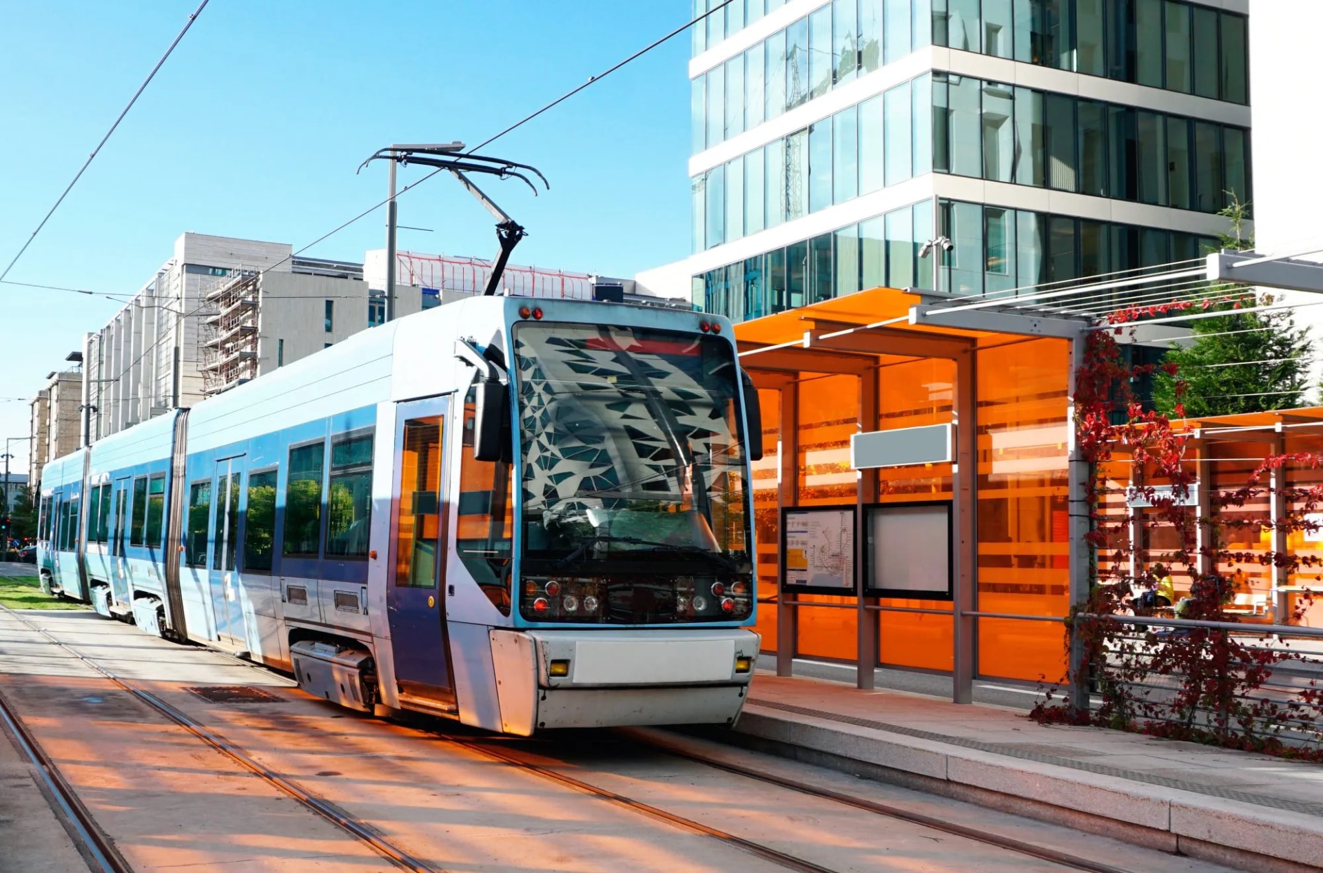 Blue and white tram stopped at modern platform with orange panels in Oslo city center.