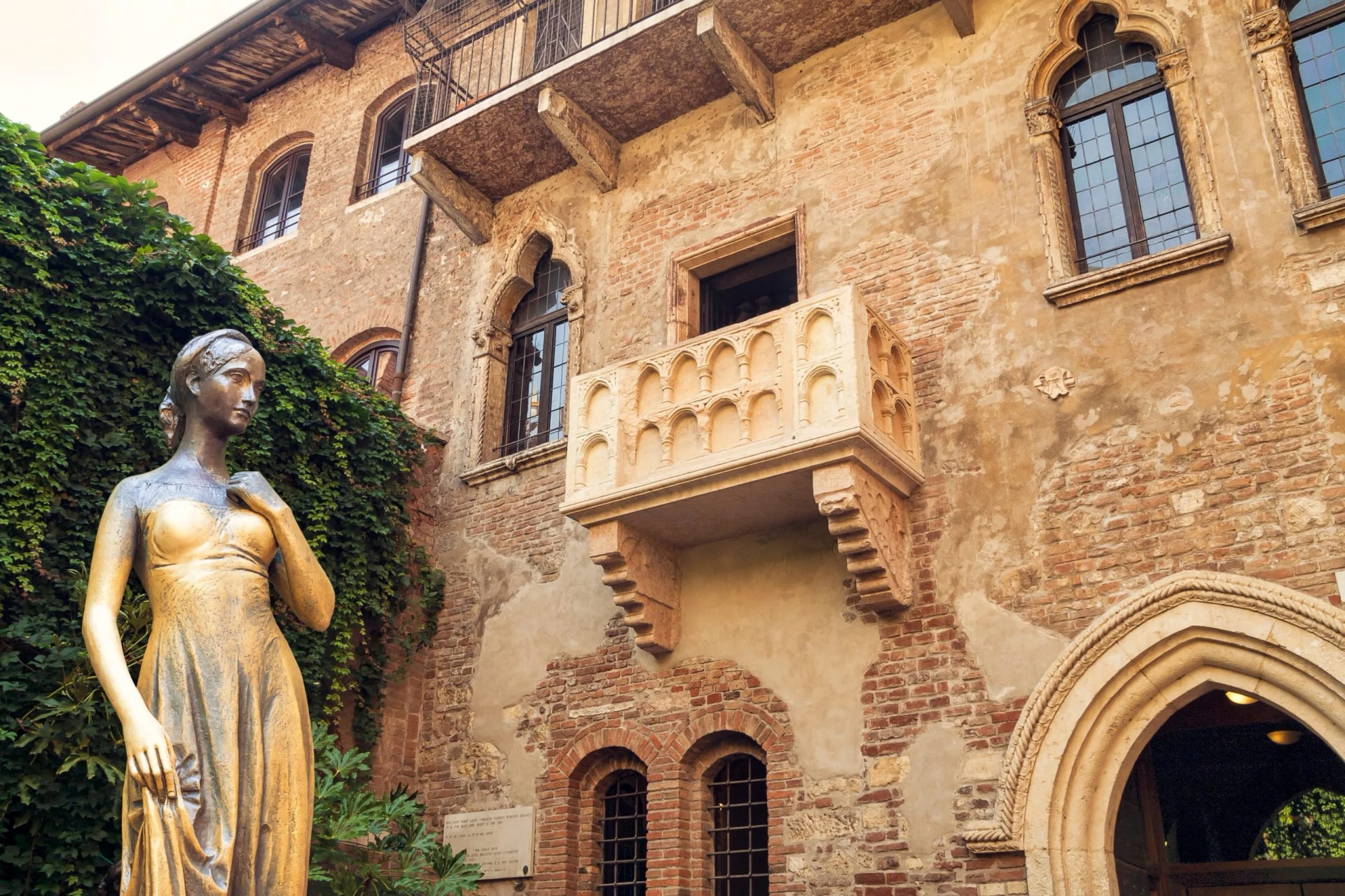Statue of Juliet next to the famous balcony on a weathered brick building in Verona.