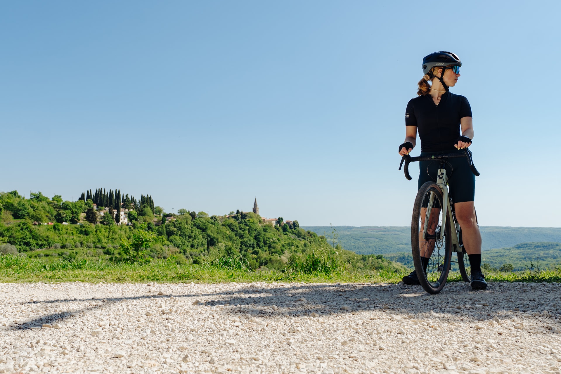 Cyclist with gravel bike resting on dirt road overlooking green hills and Istrian village.