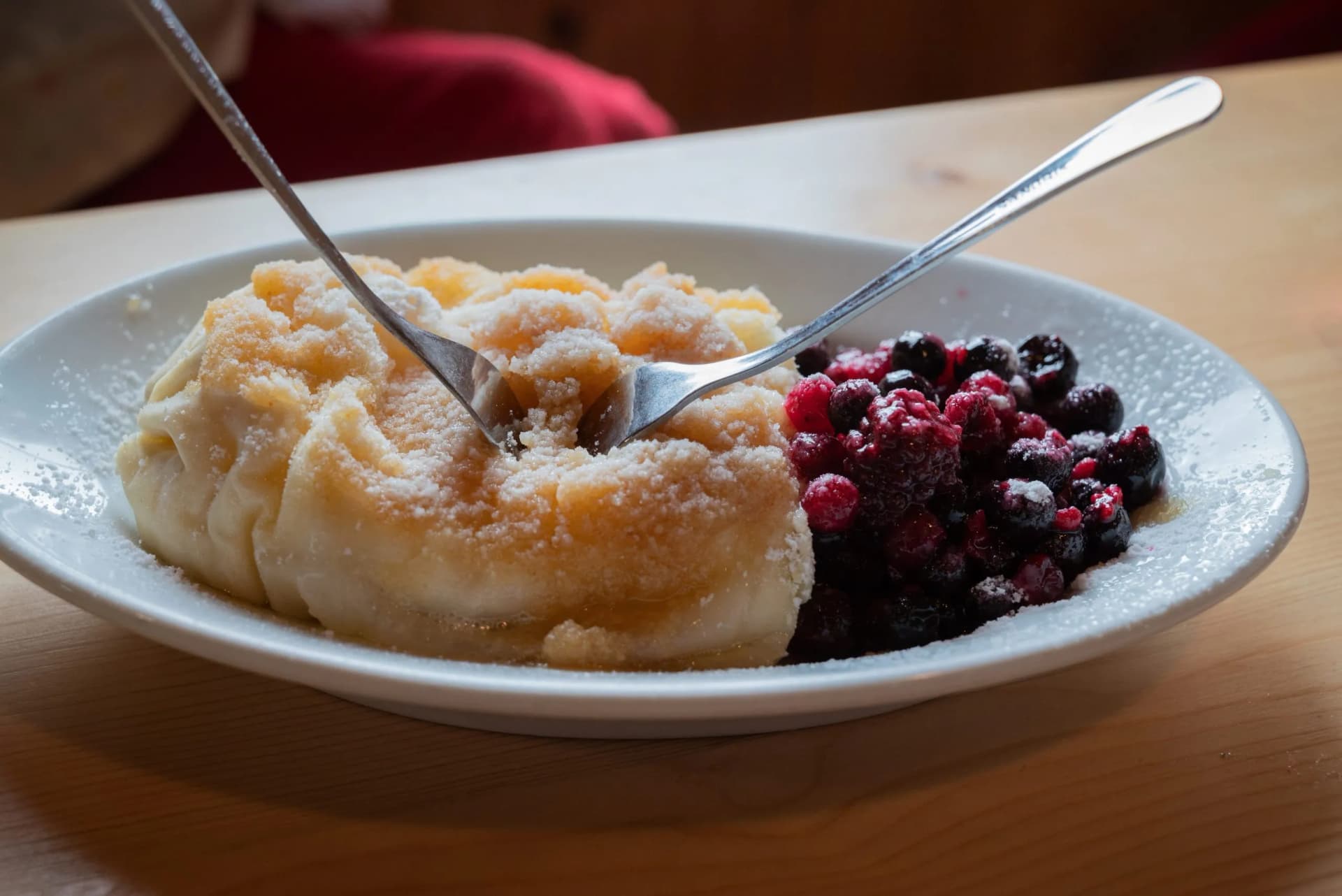 Sweet dumplings dusted with sugar served with mixed berries on a white plate with two forks.