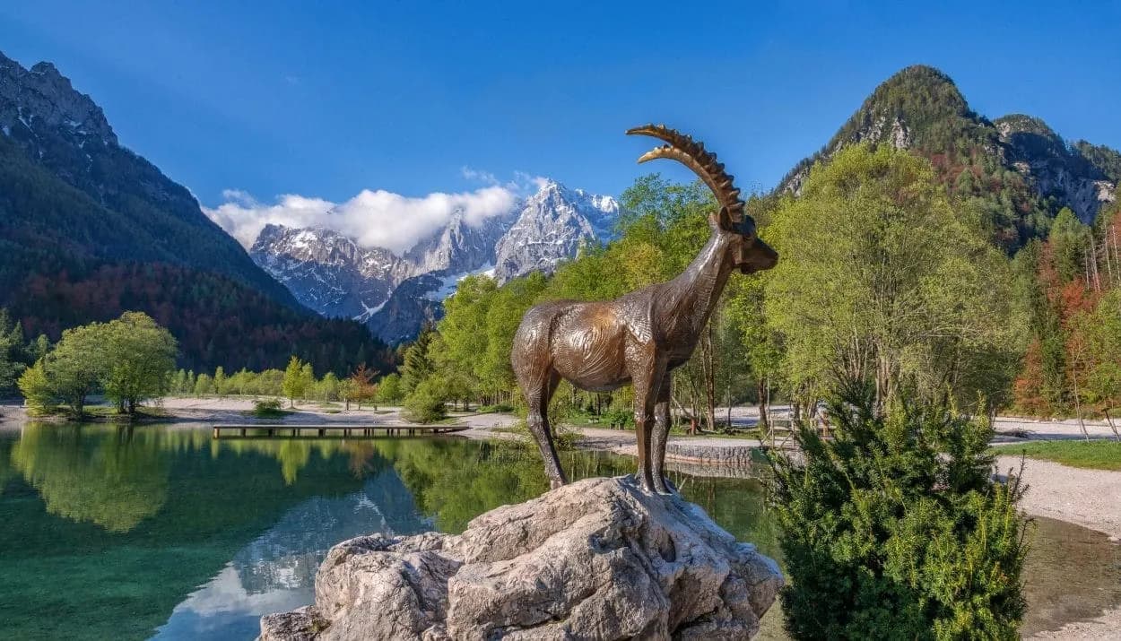 Bronze ibex statue by Lake Jasna near Kranjska Gora with snowy mountains.