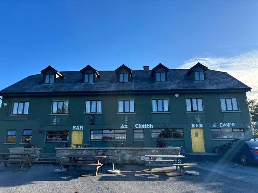 An Chéibh B&B, Bar, and Cafe building with picnic tables outside under a clear blue sky.