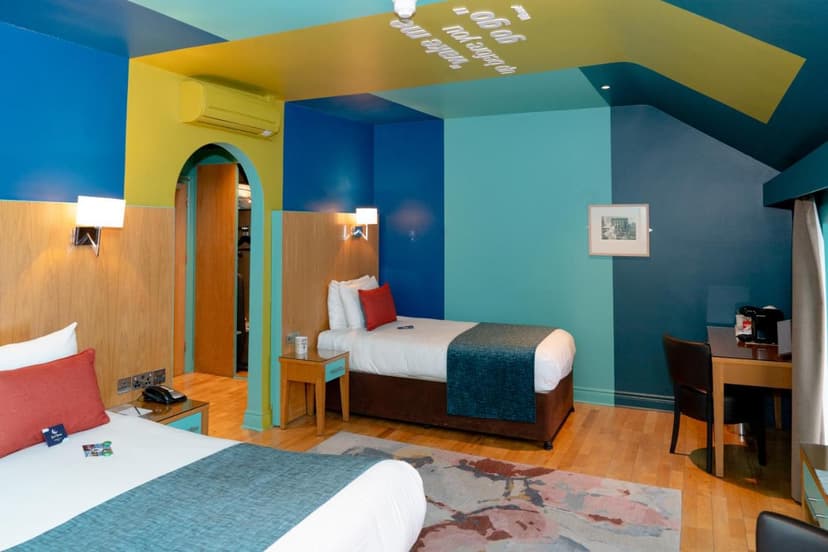 Hotel room with two beds, colorful blue and yellow walls, and wood flooring.