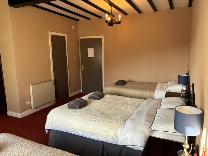 Triple bedroom in An Chéibh B&B with exposed ceiling beams and bedside lamps.