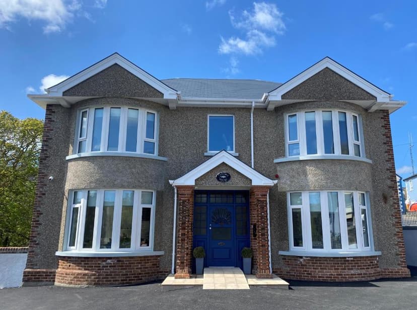 Two-story house with gray stucco and bay windows, blue front door, under blue sky.