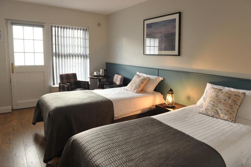 Twin beds in a hotel room with wooden floor, lantern lamp, and view through a door window.