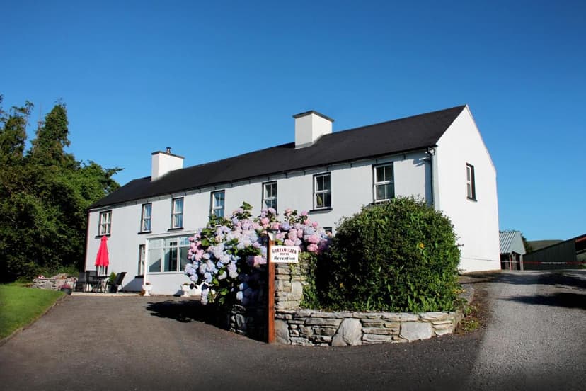 Gortamullen House reception with white walls, black roof, and large hydrangea bush under blue sky.