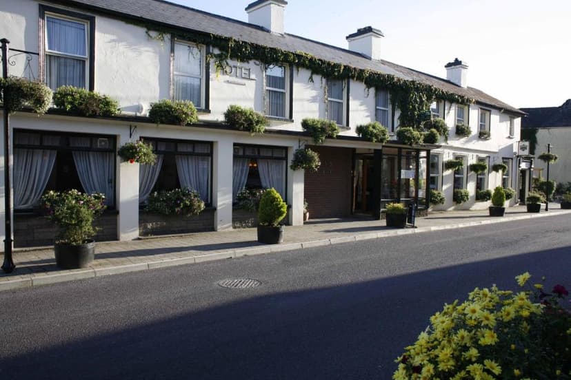 White stucco hotel exterior with dark trim, ivy, and potted plants lining a quiet street.